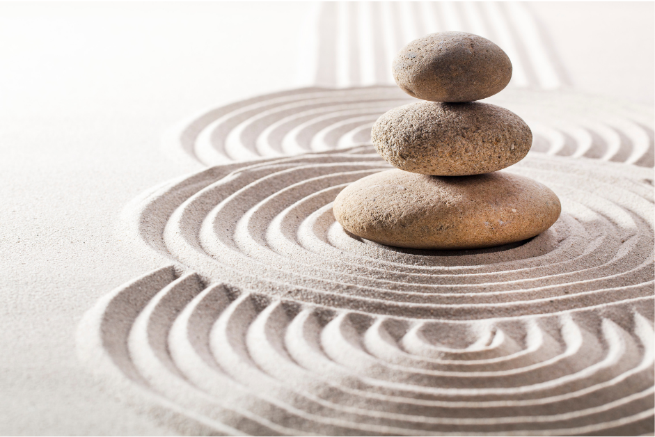 Three smooth stones balanced above flowing concentric patterns in pale sand