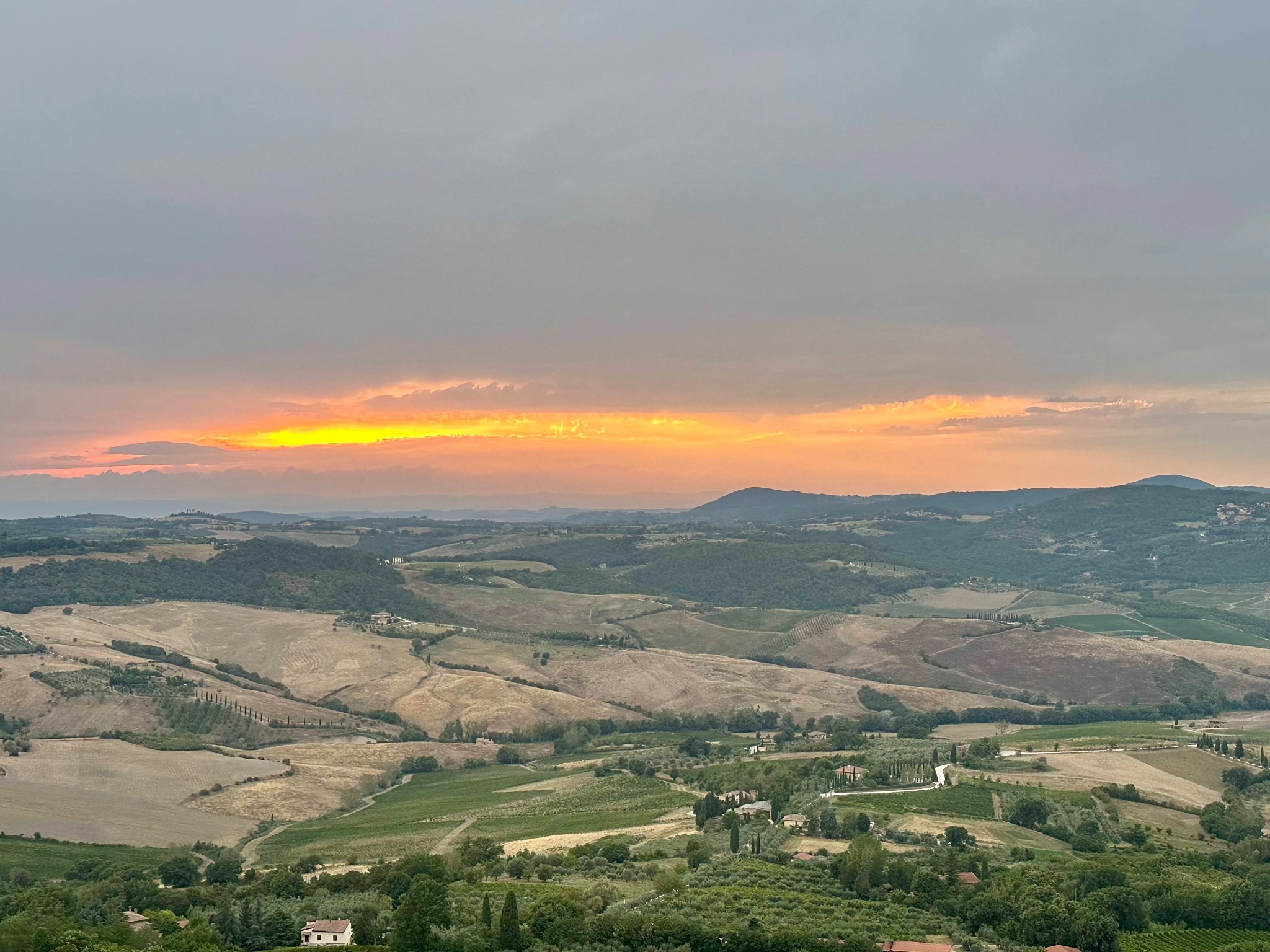 A glowing orange sunset stretching across the rolling hills and vineyards of Tuscany